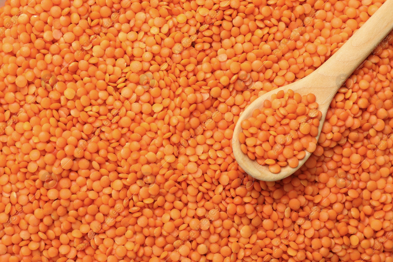 Photo of Heap of raw lentils and wooden spoon, top view. Space for text