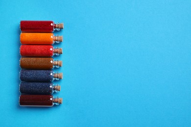 Glass bottles with different food coloring on light blue background, flat lay. Space for text