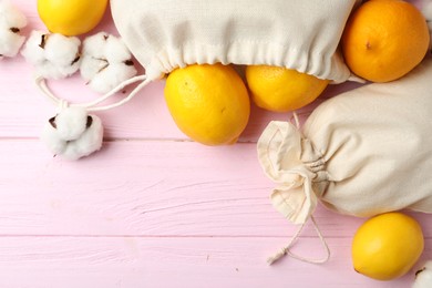 Photo of Cotton eco bags with citrus fruits on pink wooden table, flat lay