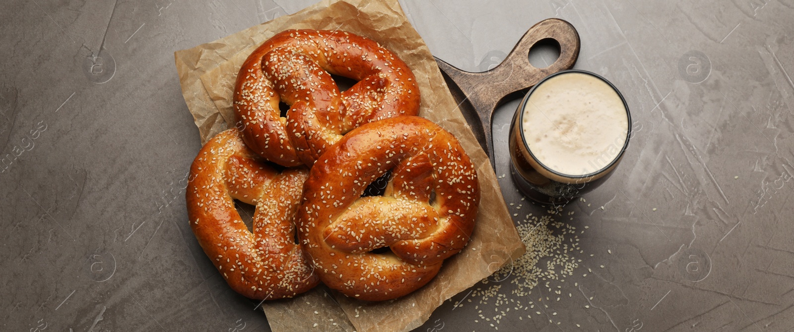 Image of Tasty pretzels and glass of beer on grey table, flat lay. Banner design