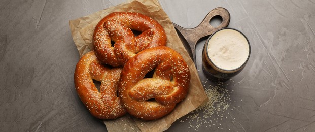 Tasty pretzels and glass of beer on grey table, flat lay. Banner design