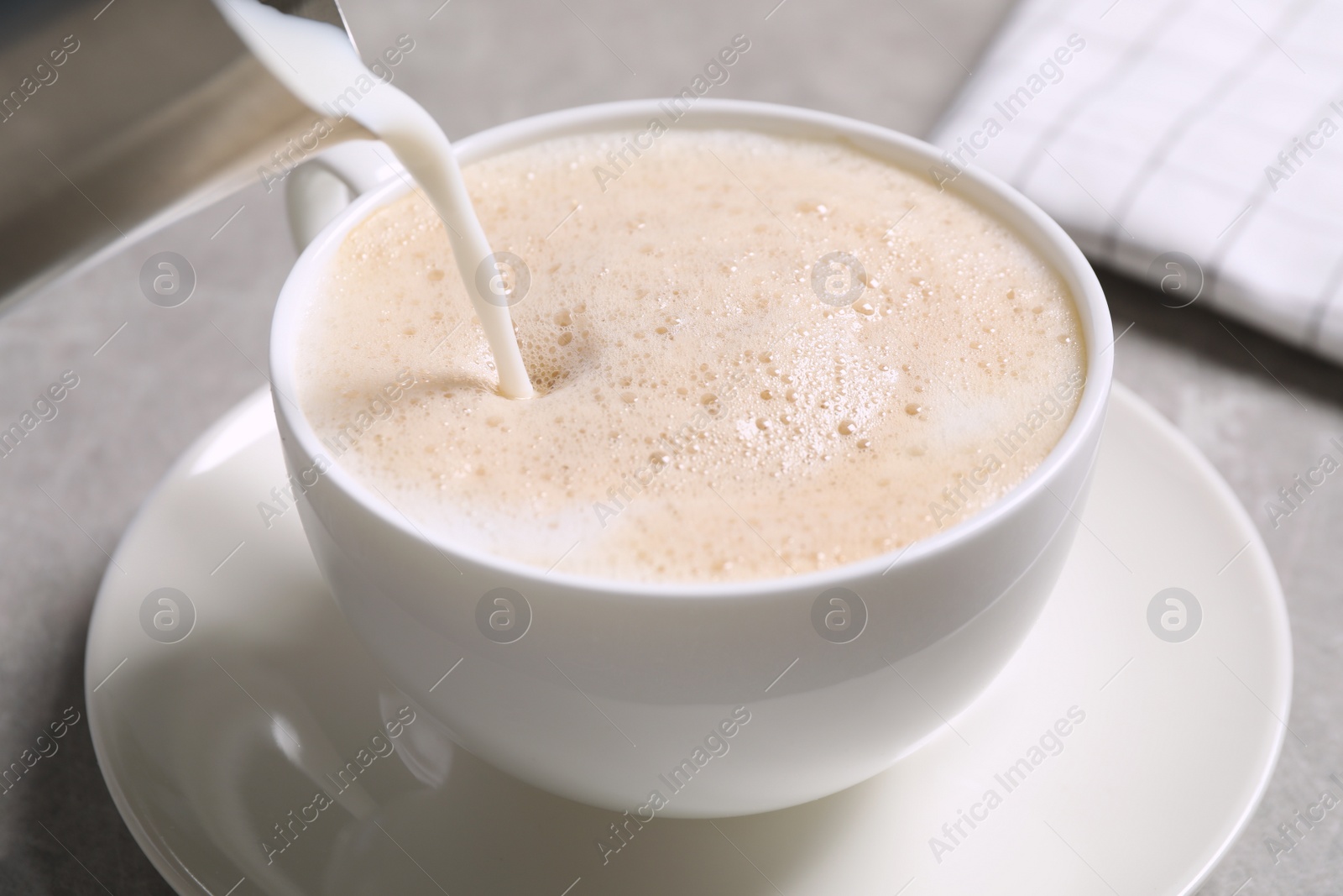 Photo of Pouring milk into cup of coffee on grey table, closeup