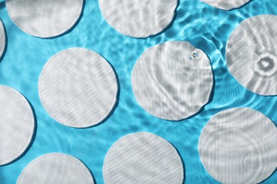 Photo of Many cotton pads in water on light blue background, flat lay