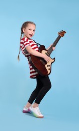 Cute girl with electric guitar on light blue background