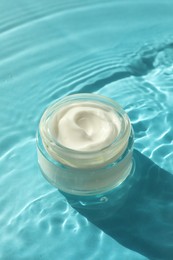 Photo of Jar with moisturizing cream in water on light blue background