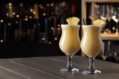 Photo of Tasty Pina Colada cocktails on wooden bar countertop, space for text