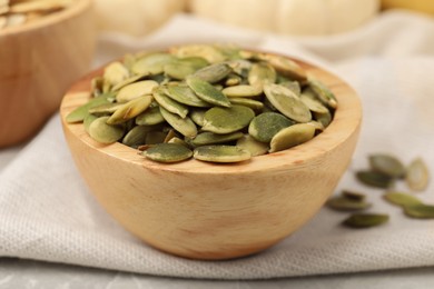 Photo of Wooden bowl with pumpkin seeds on table, closeup