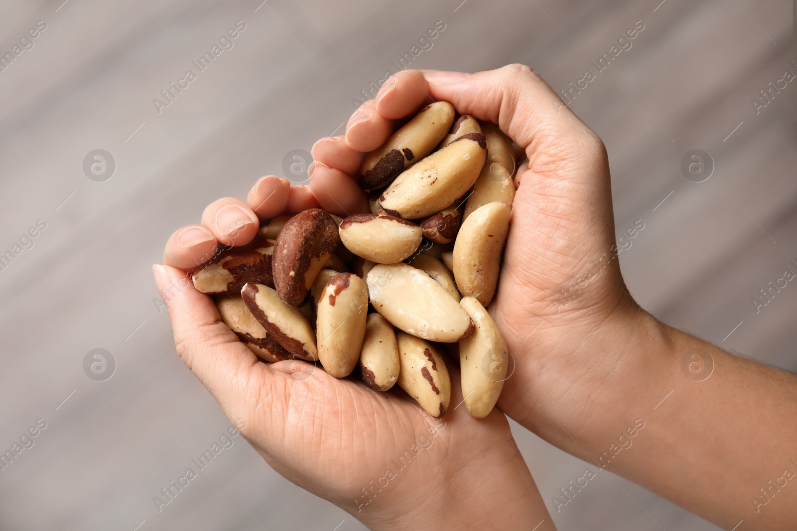 Photo of Woman holding Brazil nuts in hands on blurred background, top view