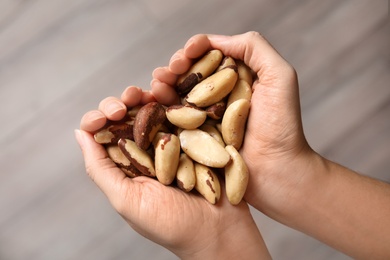 Woman holding Brazil nuts in hands on blurred background, top view