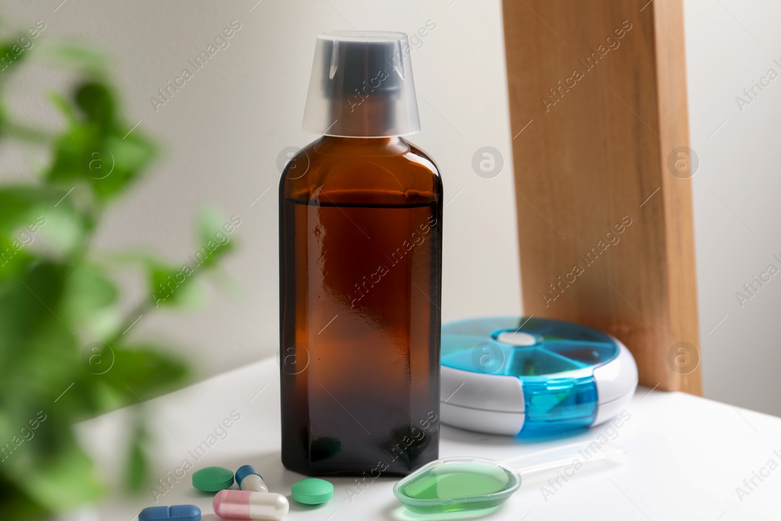 Photo of Bottle of syrup, dosing spoon and pills on shelf. Cold medicine