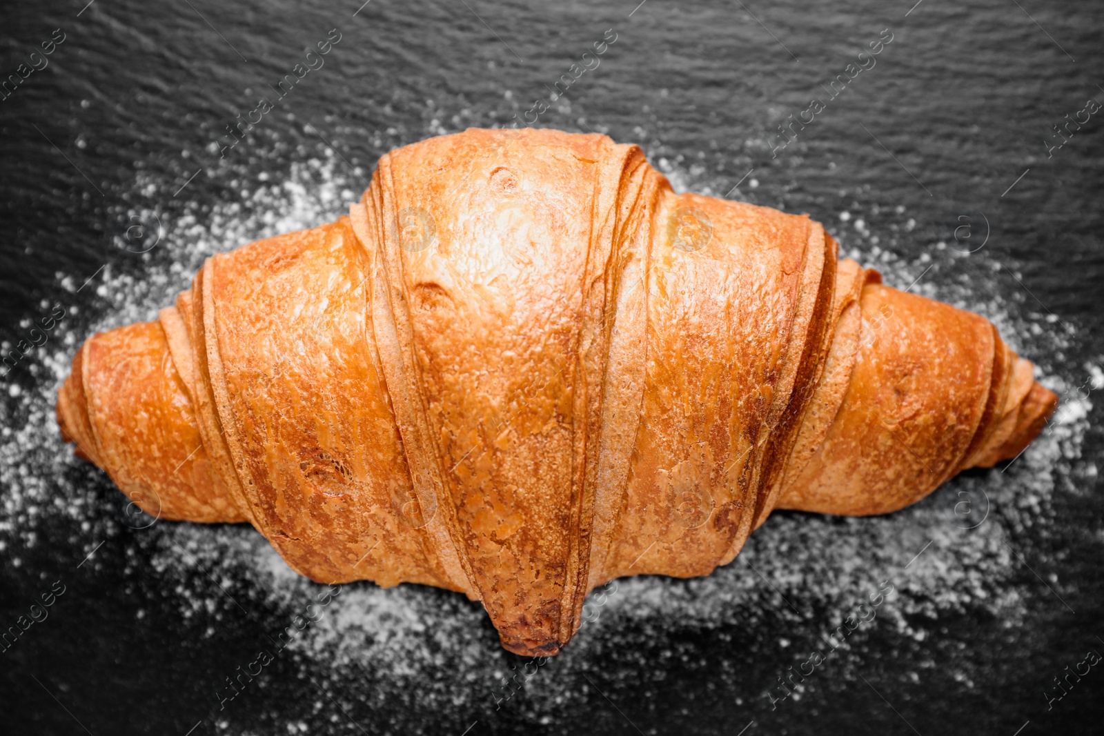 Photo of Tasty fresh croissant on black table, top view