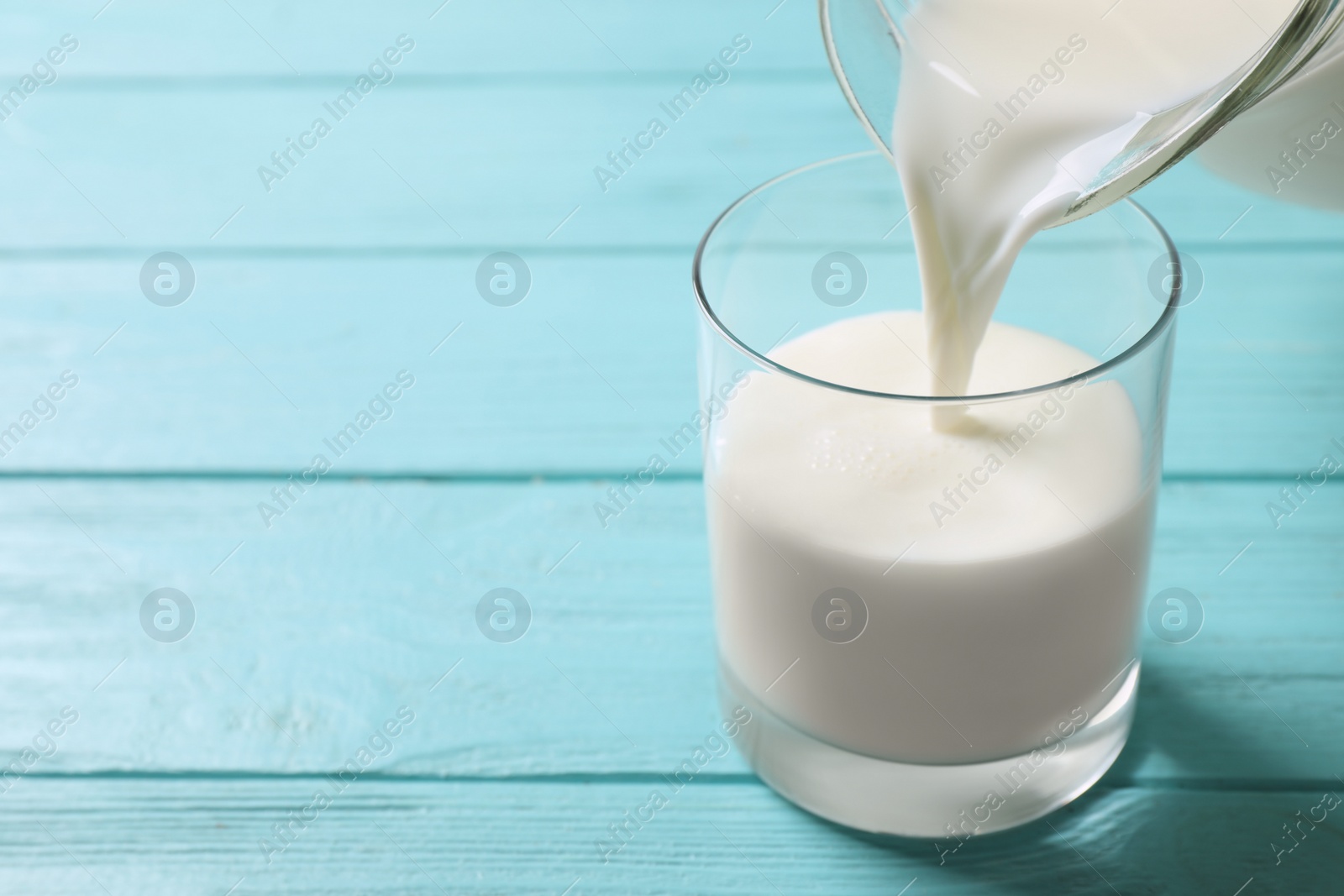 Photo of Pouring milk into glass on light blue wooden table. Space for text