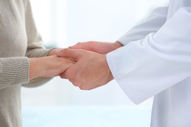 Photo of Doctor holding elderly patient hands on light background, closeup