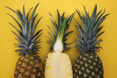 Whole and cut ripe pineapples on yellow background, flat lay