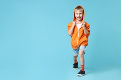 Happy little boy dancing on light blue background. Space for text