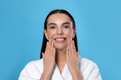 Photo of Portrait of attractive young woman in bathrobe on light blue background. Spa treatment