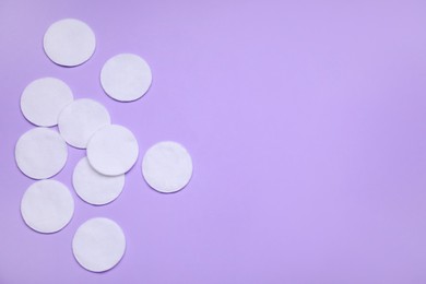 Many cotton pads on lilac background, flat lay. Space for text