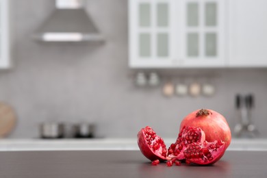 Whole and cut pomegranates on wooden counter in kitchen, space for text