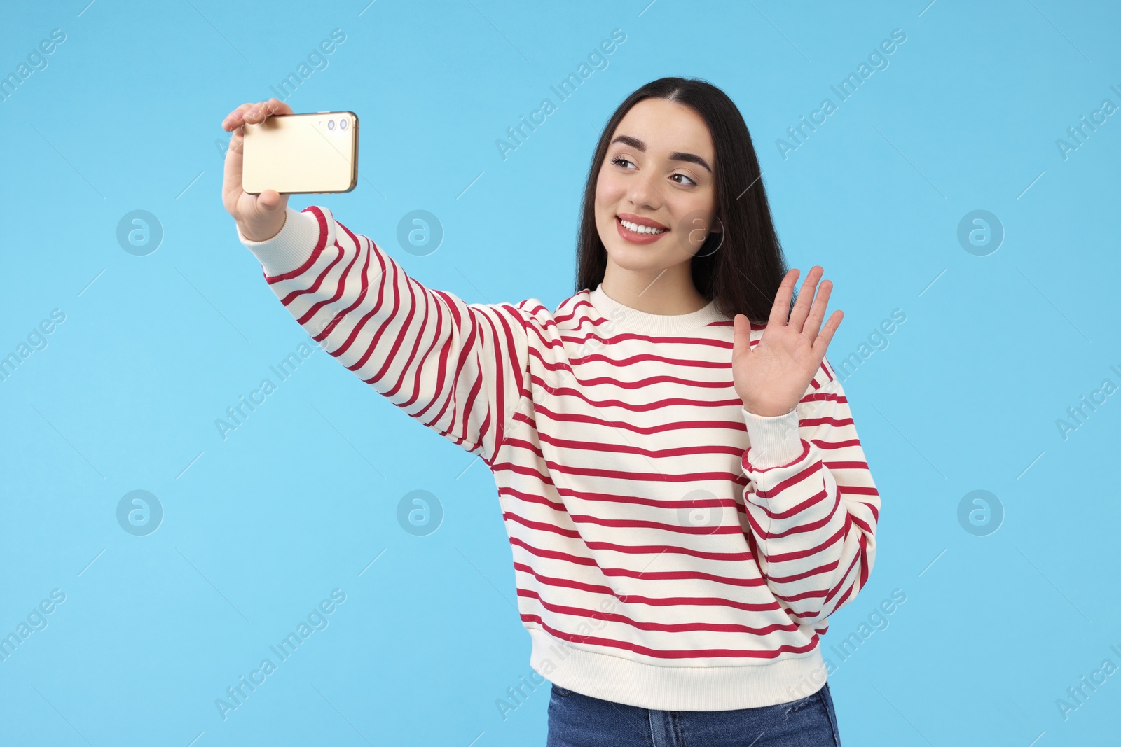 Photo of Smiling young woman taking selfie with smartphone on light blue background