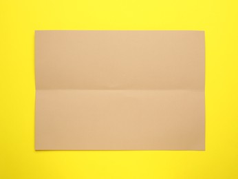 Sheet of brown paper on yellow background, top view