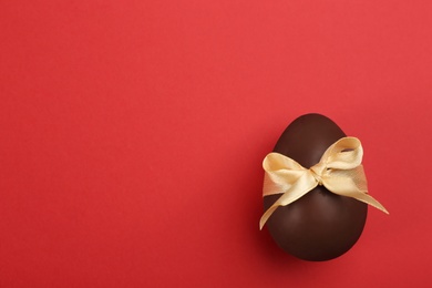 Sweet chocolate egg with beige bow on red background, top view. Space for text