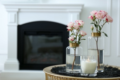 Burning candle and vases with beautiful roses on table indoors, space for text. Interior elements