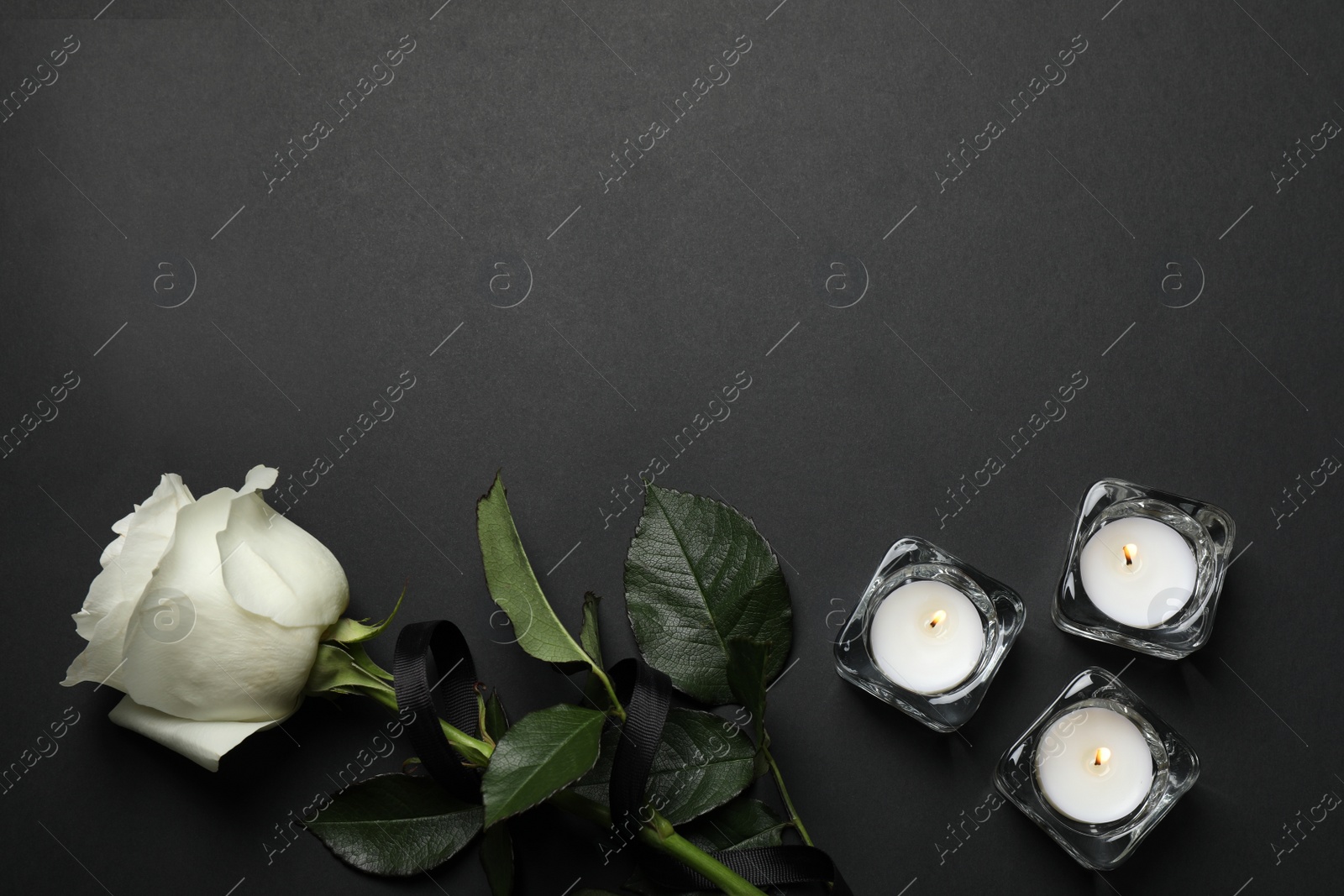 Photo of Rose with black ribbon and candles on dark background, flat lay. Space for text