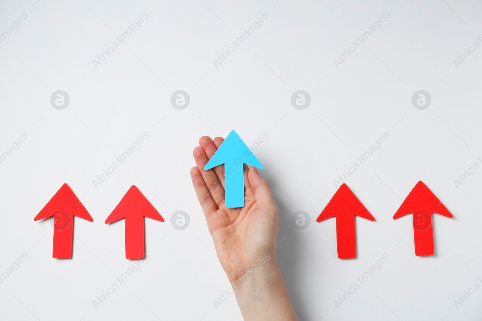 Photo of Woman holding light blue paper arrow among red arrows on white background, top view. Space for text