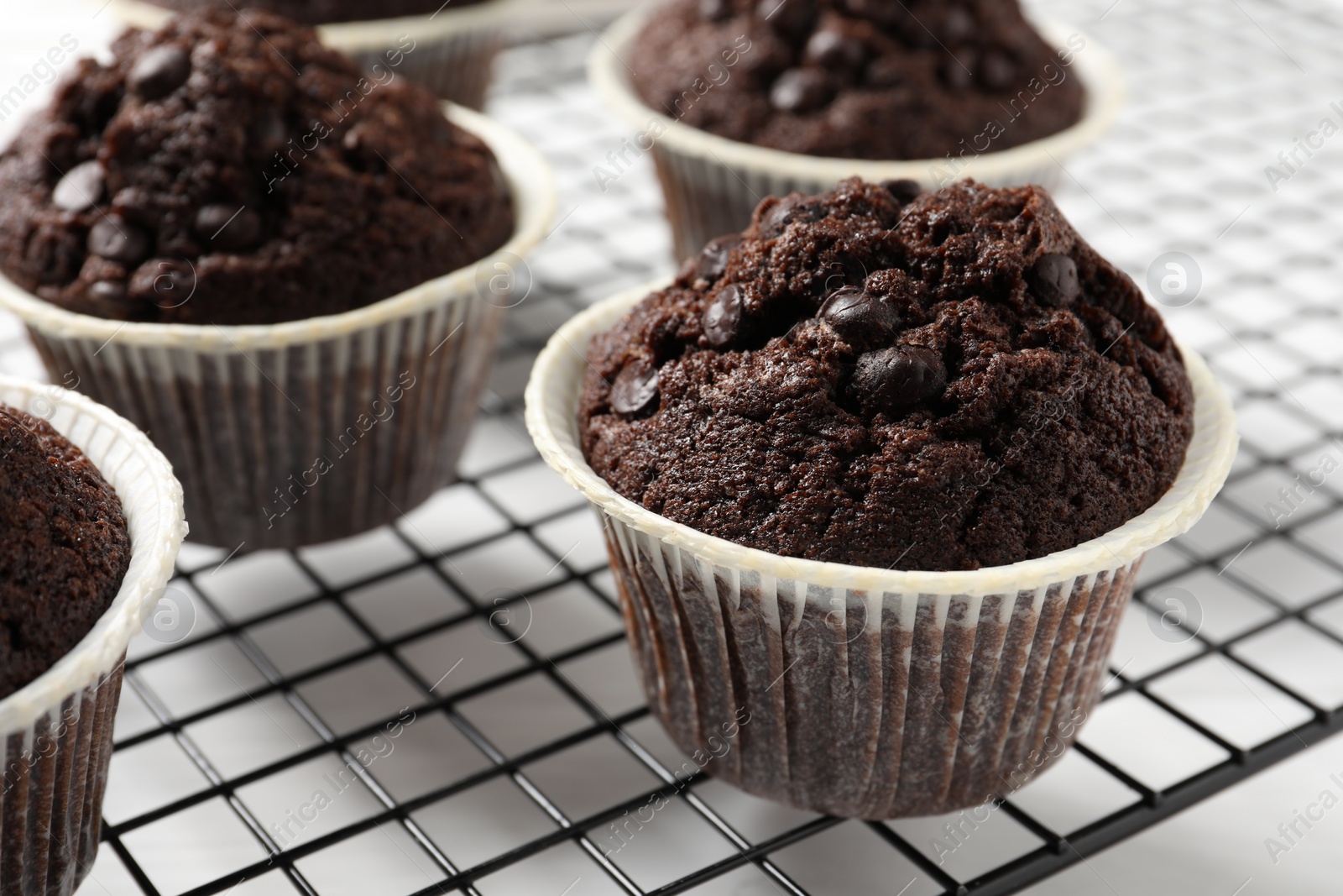 Photo of Tasty chocolate muffins and cooling rack on white table, closeup