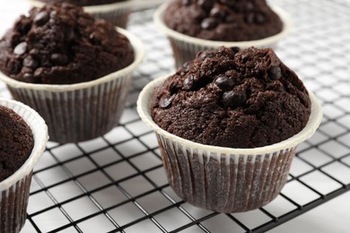 Tasty chocolate muffins and cooling rack on white table, closeup