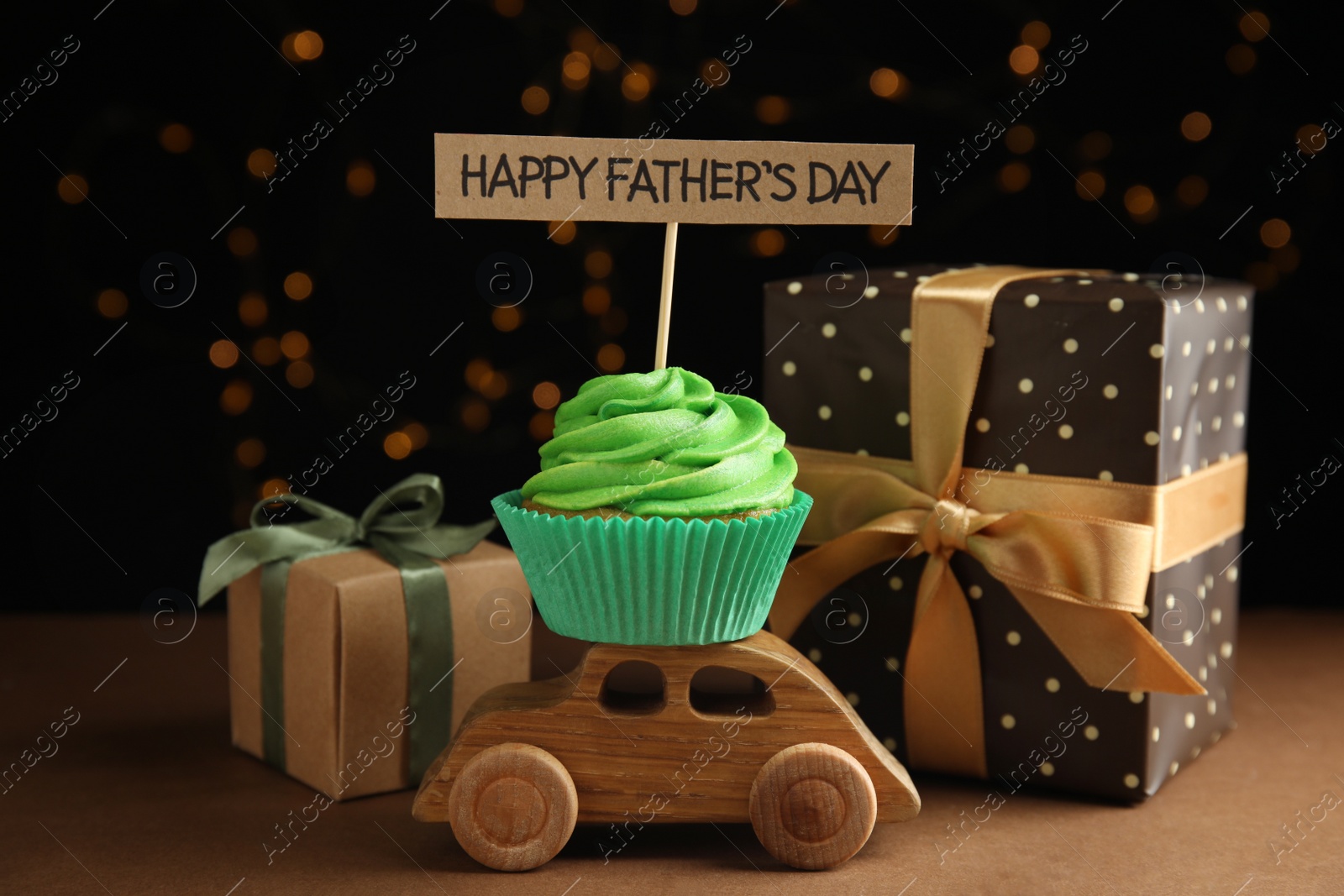 Photo of Composition with cupcake and gift boxes on brown table against blurred lights. Happy Father's day