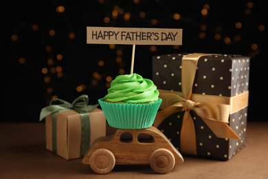 Photo of Composition with cupcake and gift boxes on brown table against blurred lights. Happy Father's day