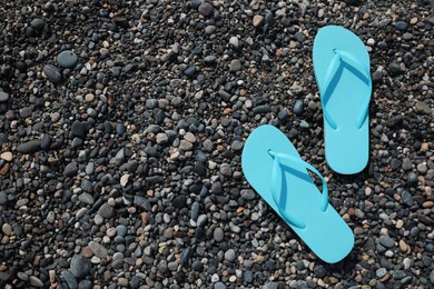 Stylish turquoise flip lops on pebble beach, flat lay. Space for text