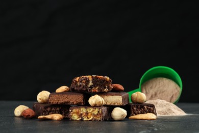 Photo of Different tasty energy bars, nuts and protein powder on black table