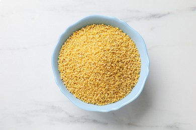 Photo of Millet groats in bowl on white marble table, top view