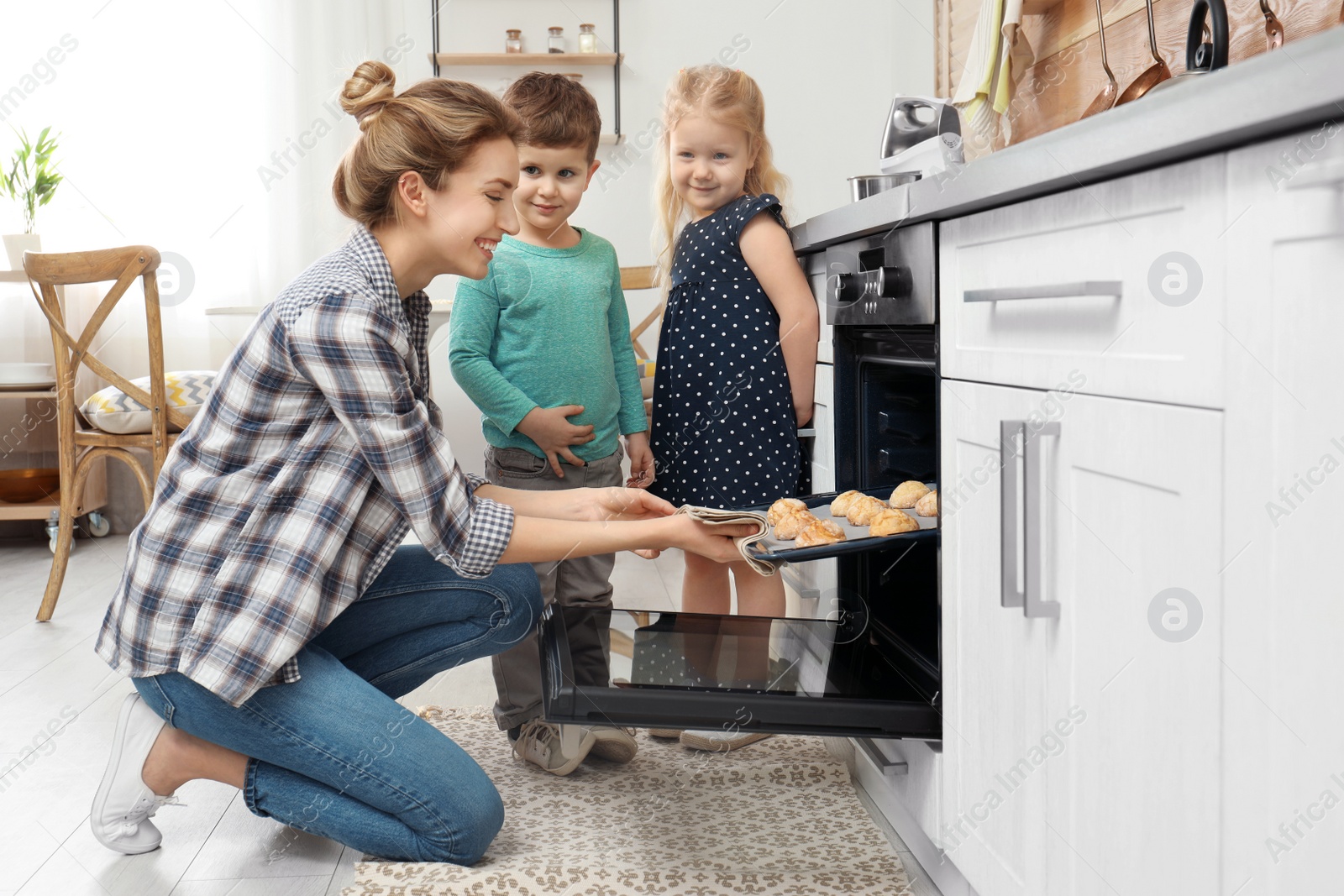 Photo of Mother and her children taking out cookies from oven in kitchen