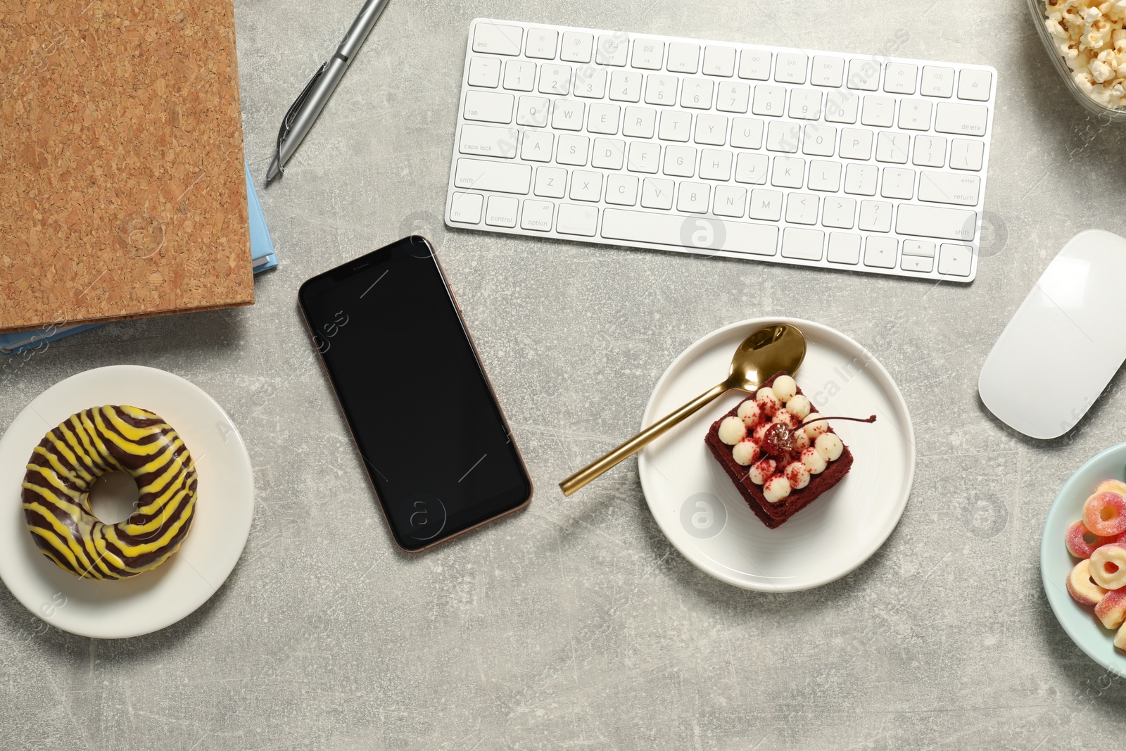 Photo of Bad eating habits at workplace. Keyboard, smartphone and different snacks on light grey table, flat lay