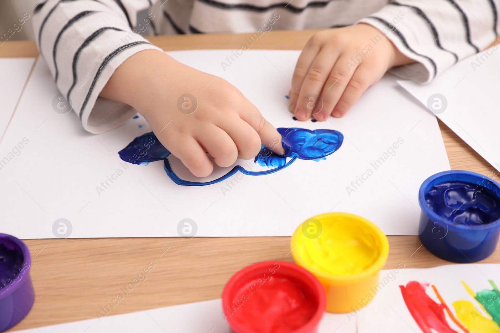 Photo of Little child painting with finger at wooden table , closeup