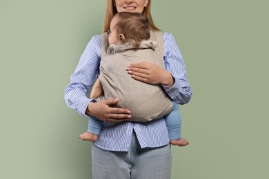 Mother holding her child in sling (baby carrier) on olive background, closeup