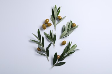 Twigs with olives and fresh green leaves on white background, flat lay