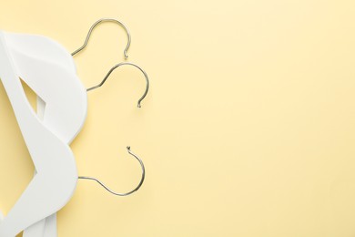 Photo of White hangers on pale yellow background, top view. Space for text