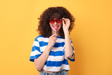 Photo of Beautiful woman in sunglasses with lollipop on yellow background