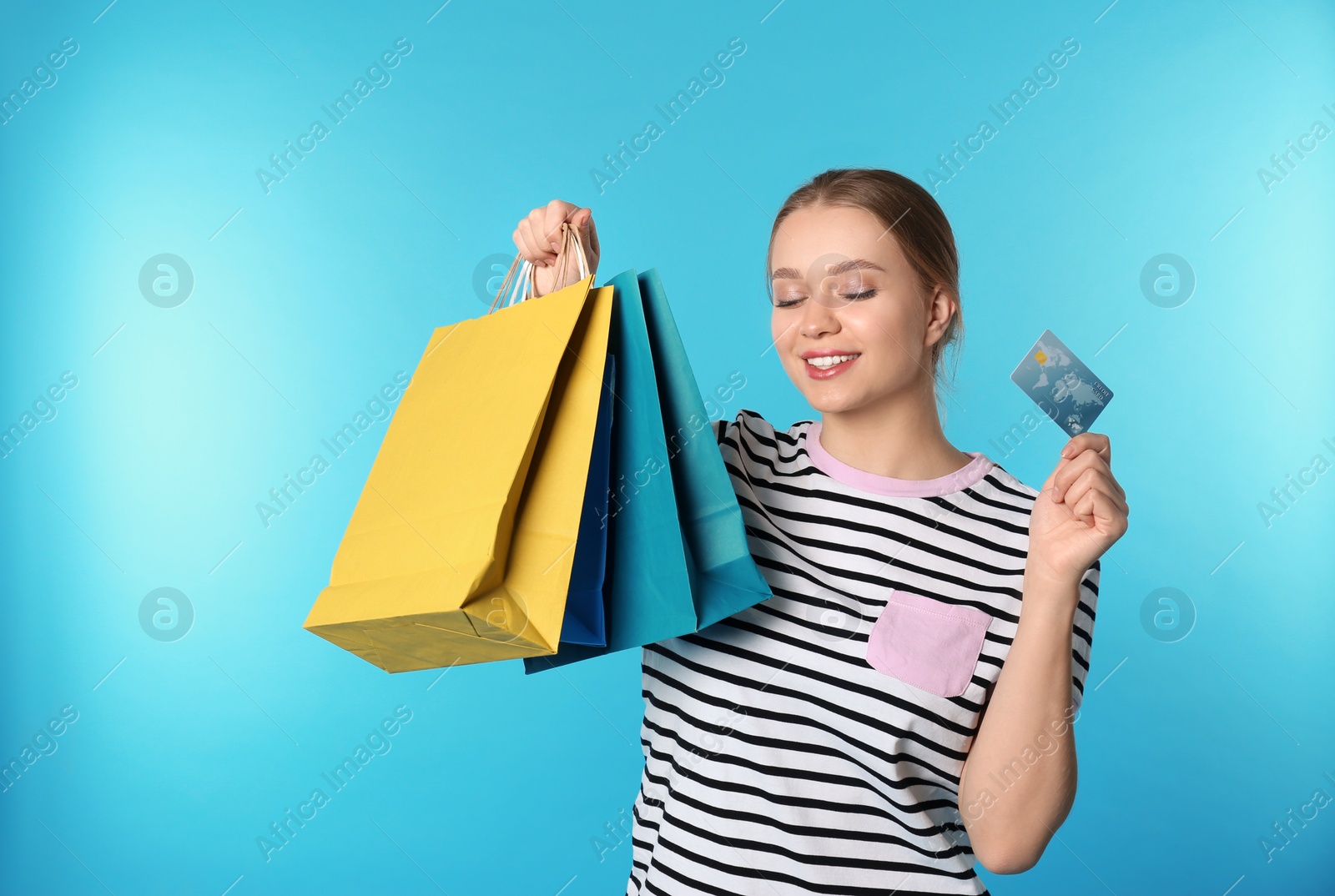 Photo of Portrait of happy young woman with credit card and shopping bags on color background. Spending money