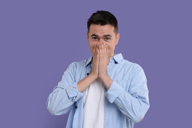 Photo of Embarrassed man covering mouth with hands on violet background