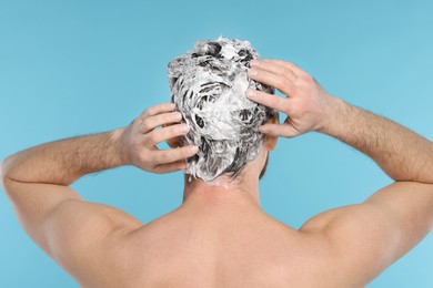 Man washing his hair with shampoo on light blue background, back view