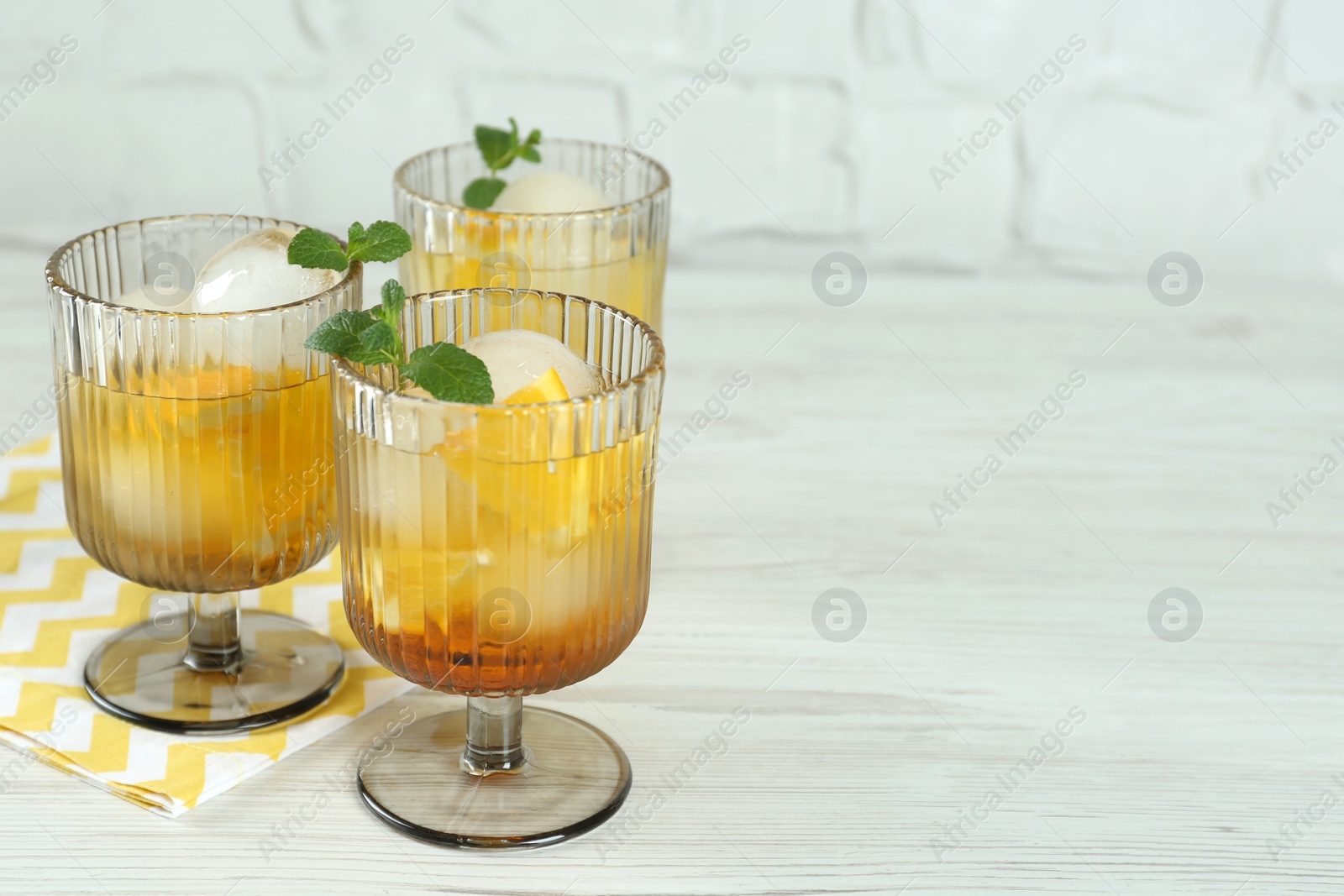 Photo of Delicious cocktails with orange, mint and ice balls on white wooden table, space for text