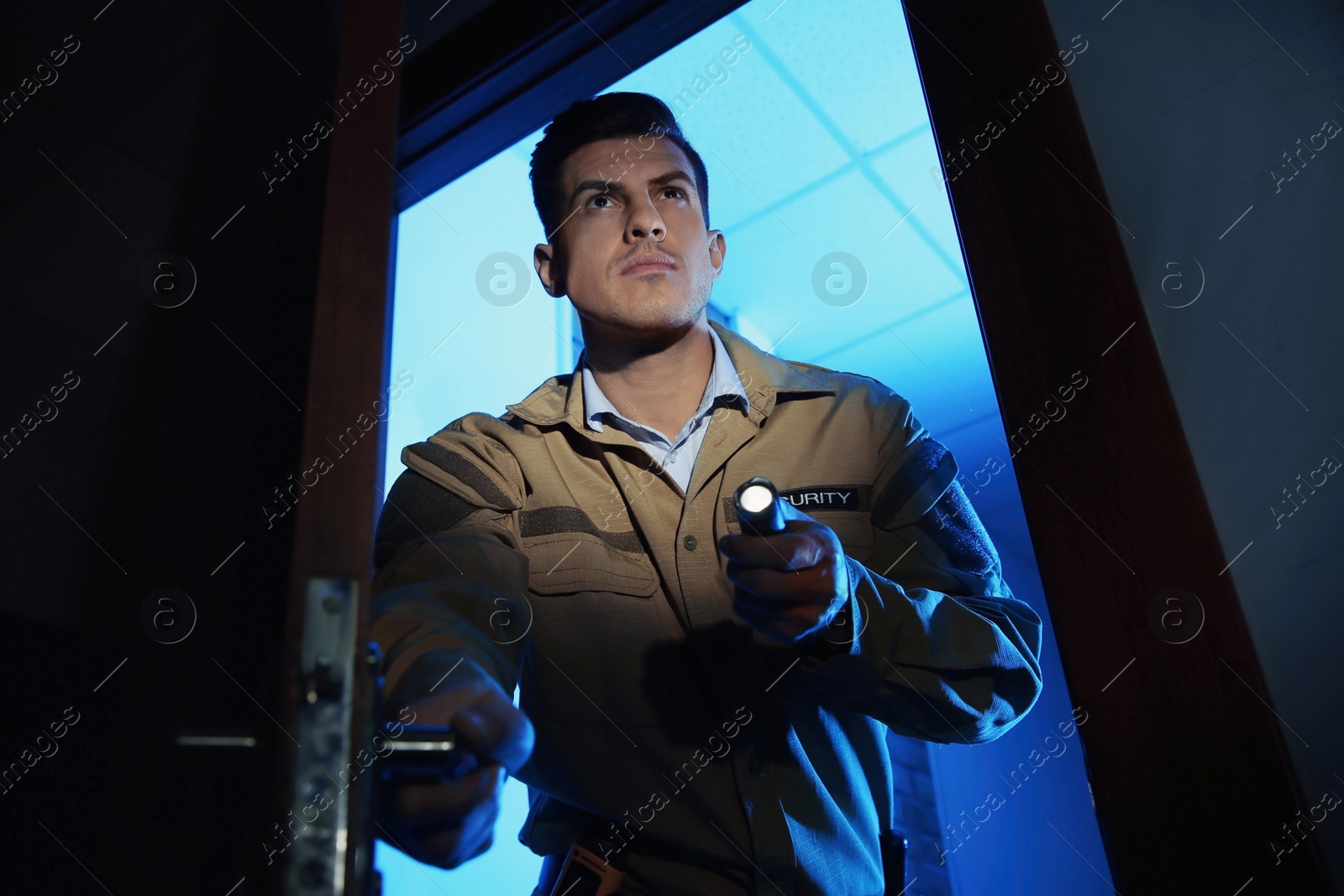 Photo of Professional security guard with flashlight checking dark room