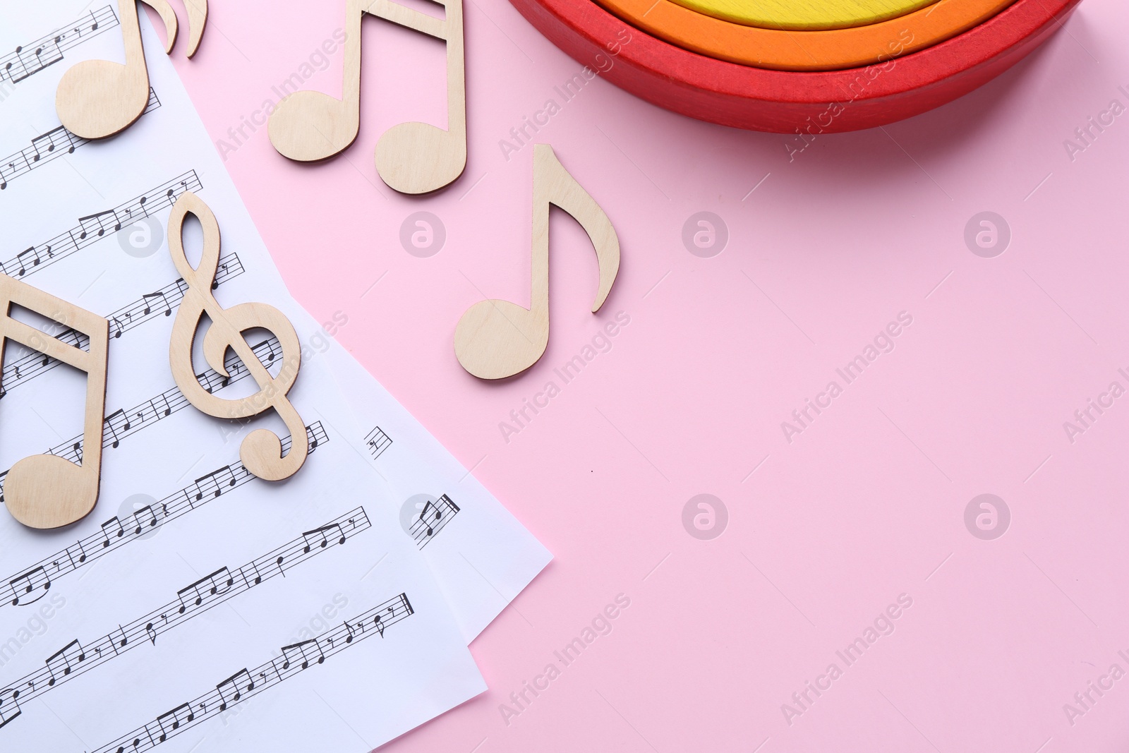 Photo of Baby songs. Music sheets, wooden notes and toy rainbow on pink background, flat lay with space for text