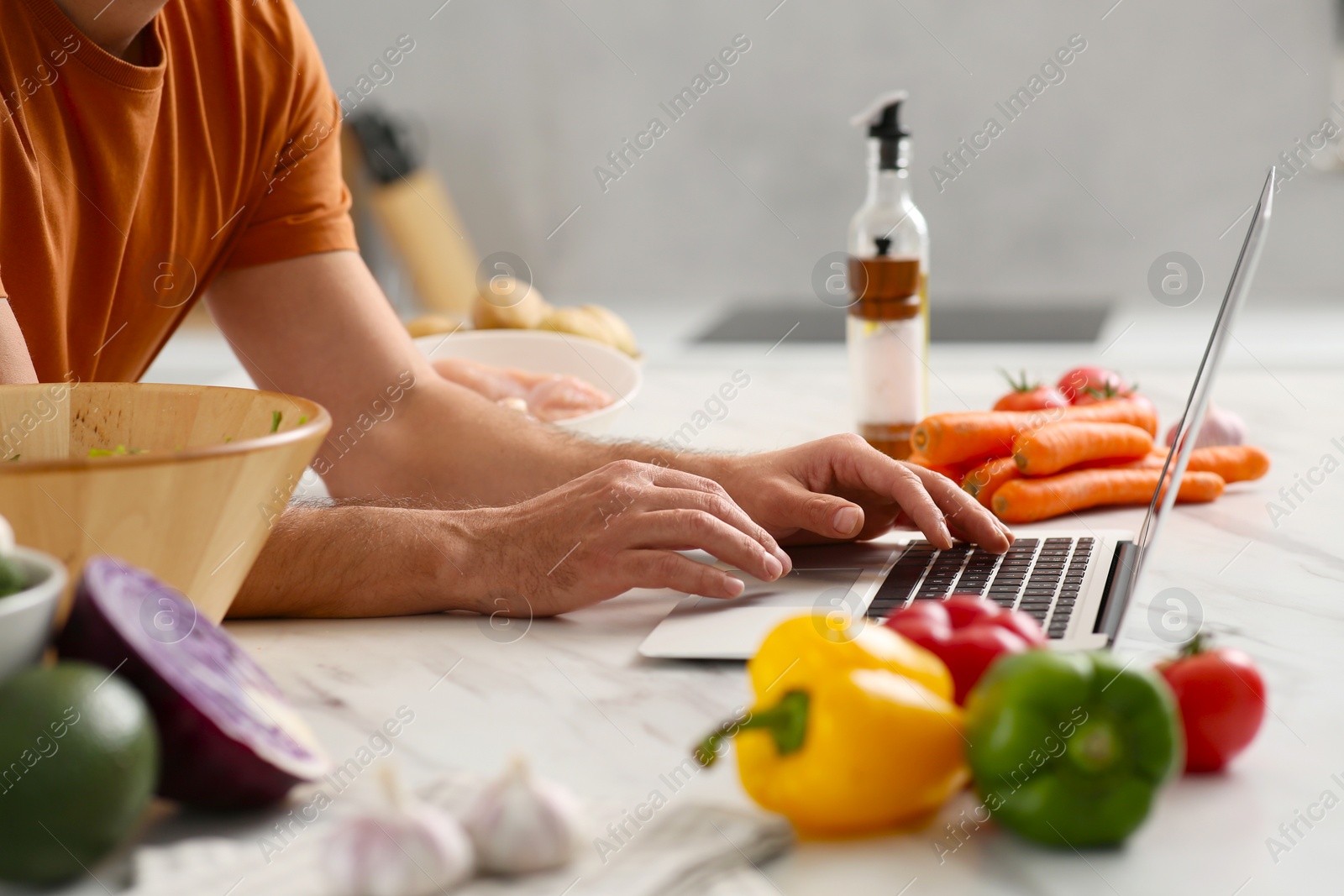 Photo of Man making dinner while watching online cooking course via laptop in kitchen, closeup