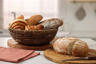 Wicker bread basket with freshly baked loaves and knife on white marble table in kitchen